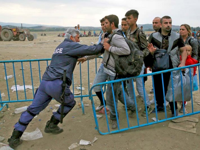 A Greek policeman pushes refugees behind a barrier at Greece’s border with Macedonia, near the Greek village of Idomeni. (© Yannis Behrakis/Reuters)